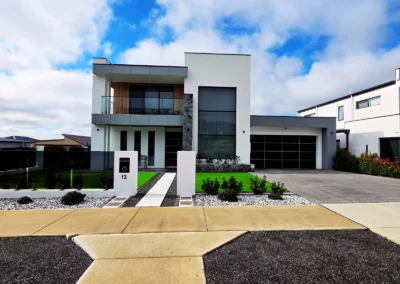 Modern two-story white house with large windows, a balcony, and a gray driveway