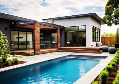 Modern house with large windows, wooden patio, and rectangular pool under a partly cloudy sky