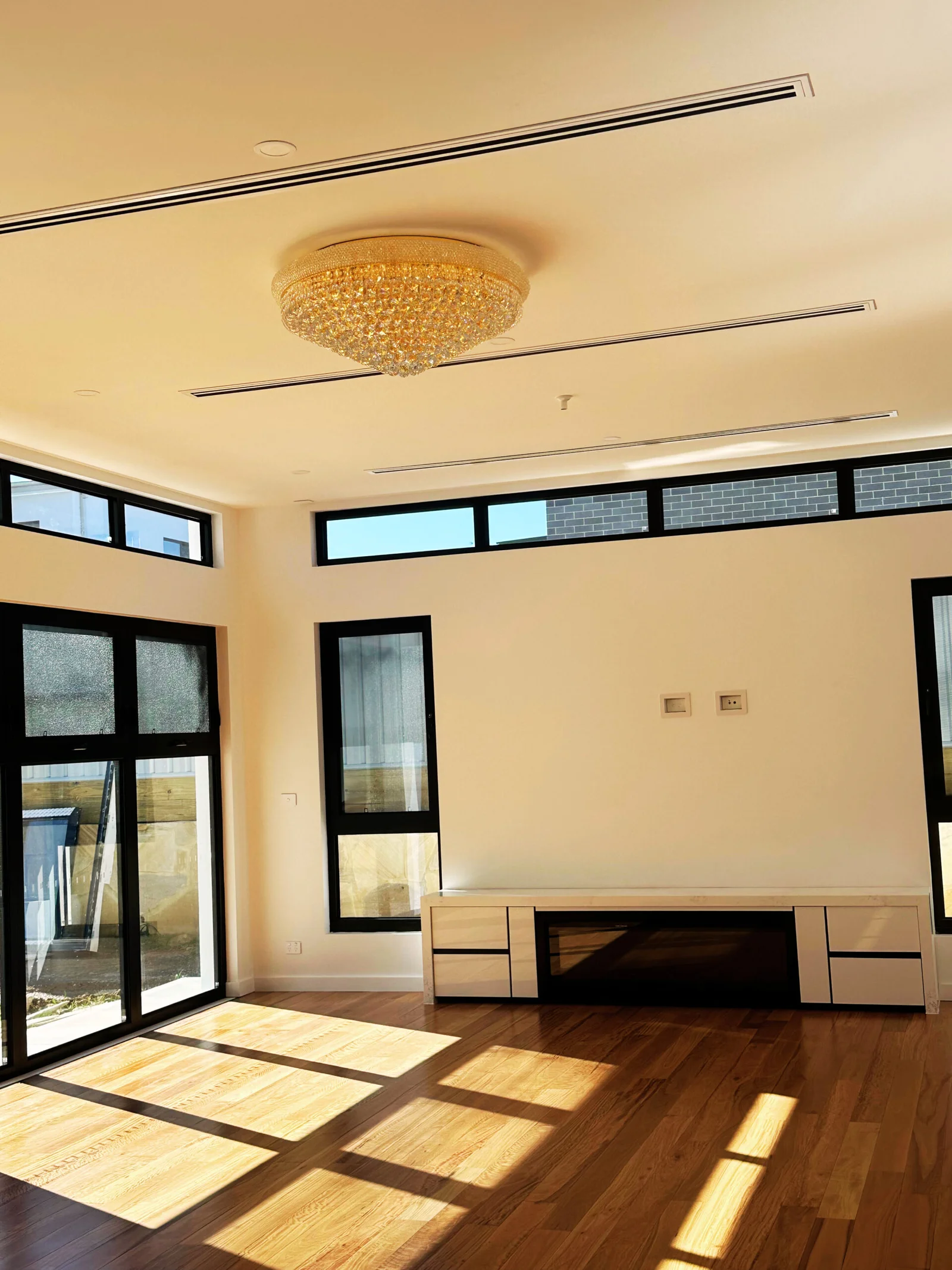 A spacious, sunlit room with light wood flooring and large black-framed windows